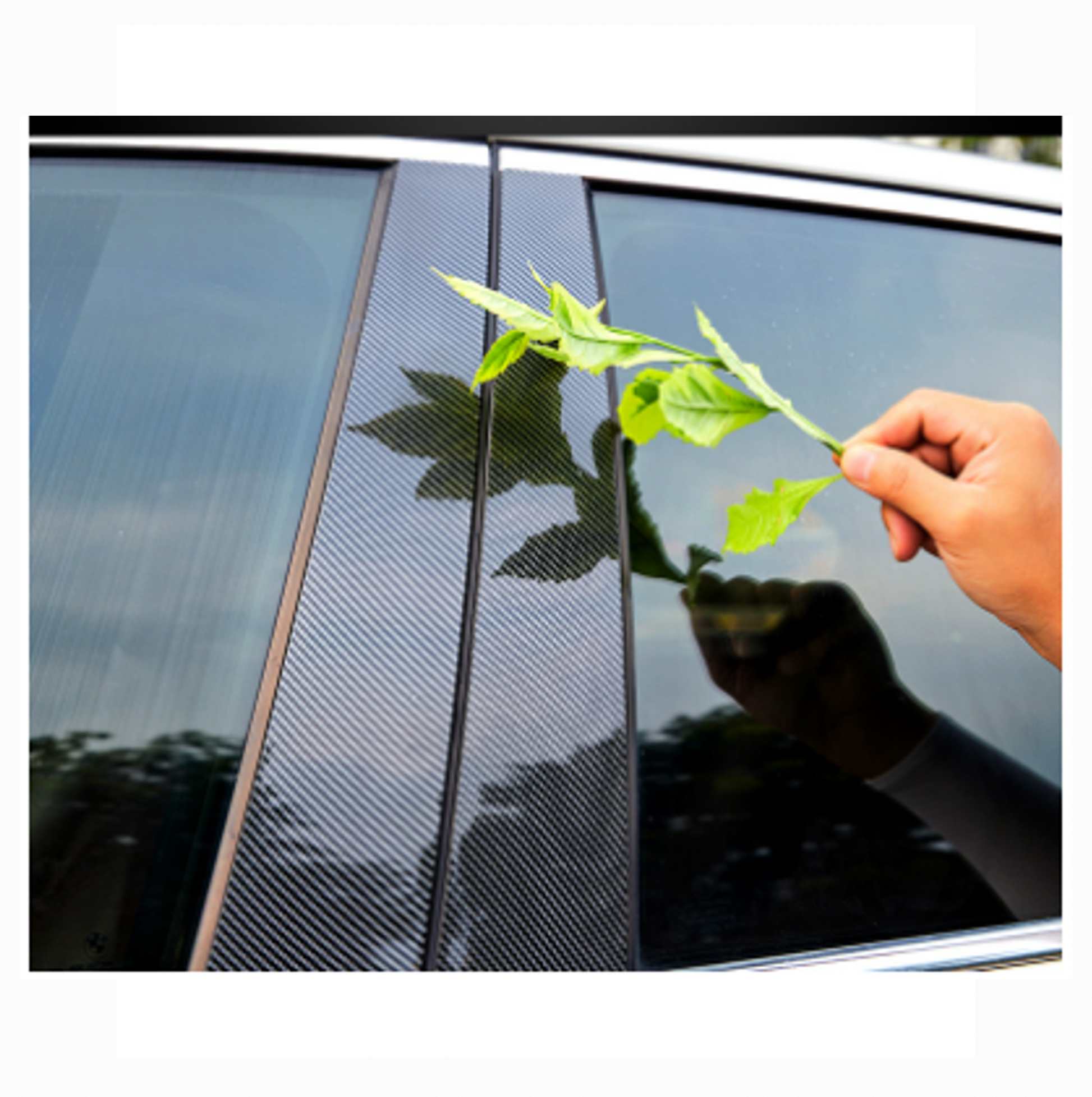 Hand touching carbon fiber texture B-pillar trim on BYD vehicle, showing glossy finish and scratch resistance, with green leaf held nearby.